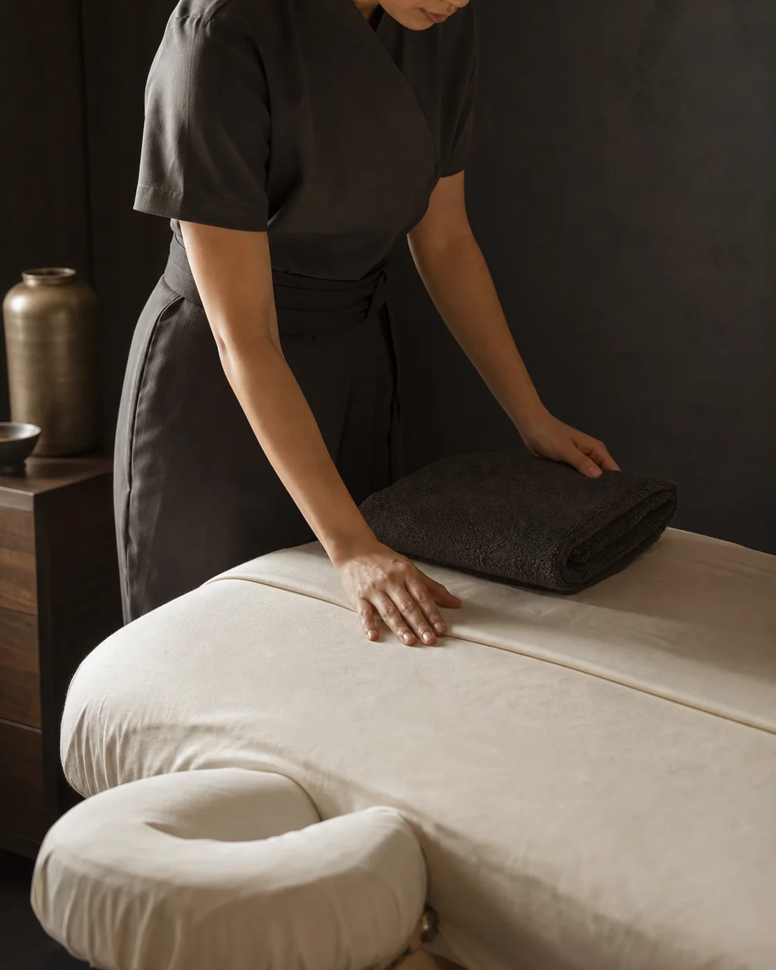 A therapist preparing a massage table with clean linens