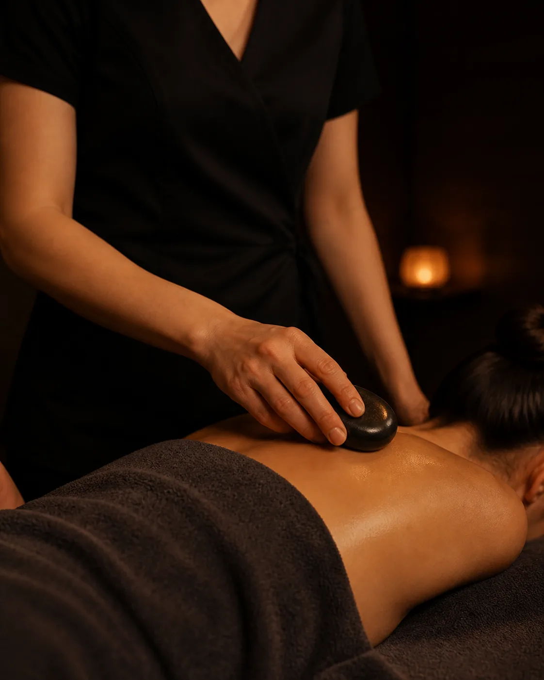 A therapist working a heated stone across the shoulder