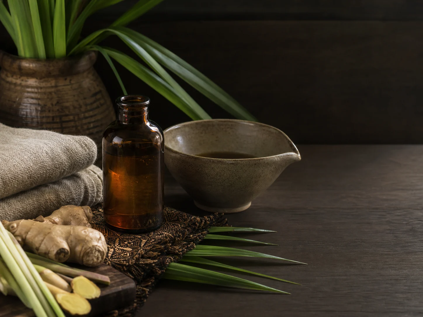Unlabelled massage oil, linen and botanical ingredients prepared on a timber table